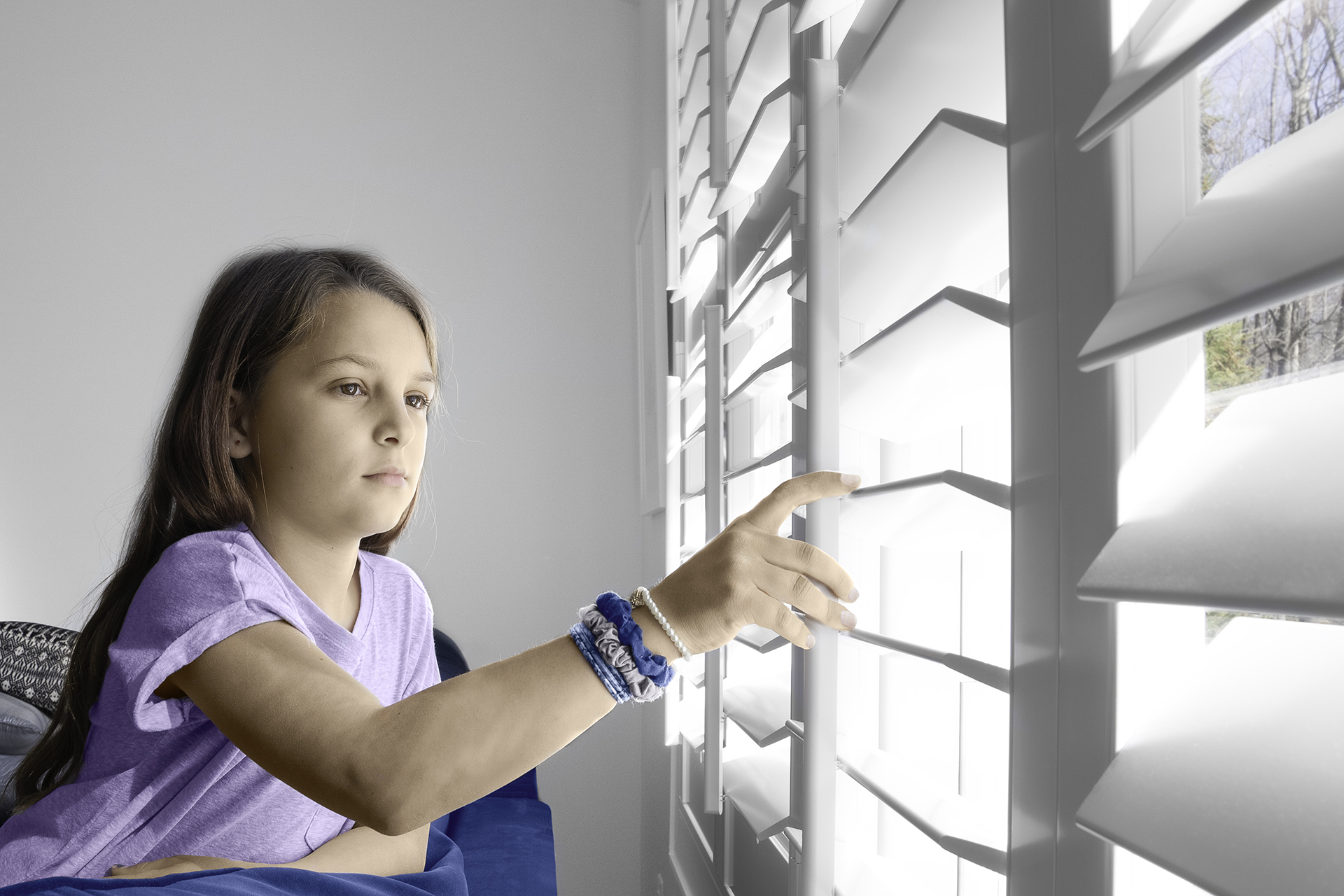 A young girl reaches out to touch the louvers on indoor shutters