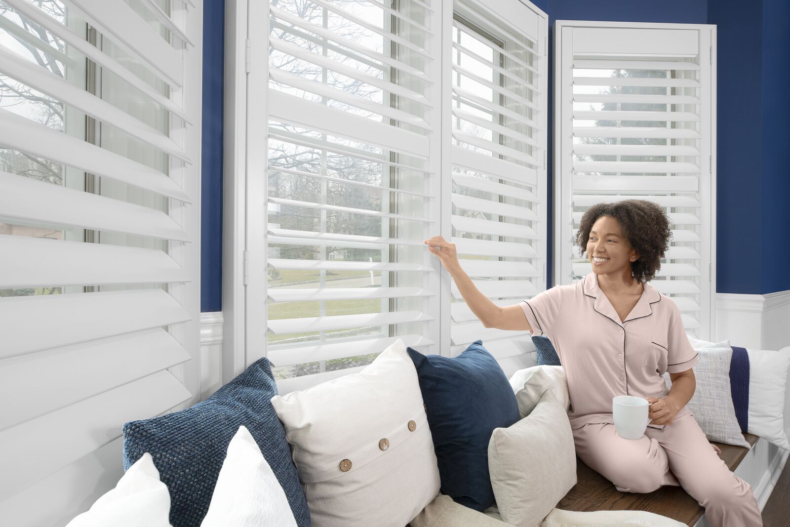 A woman smiles as she adjusts the slats of the indoor shutters on a large bay window.