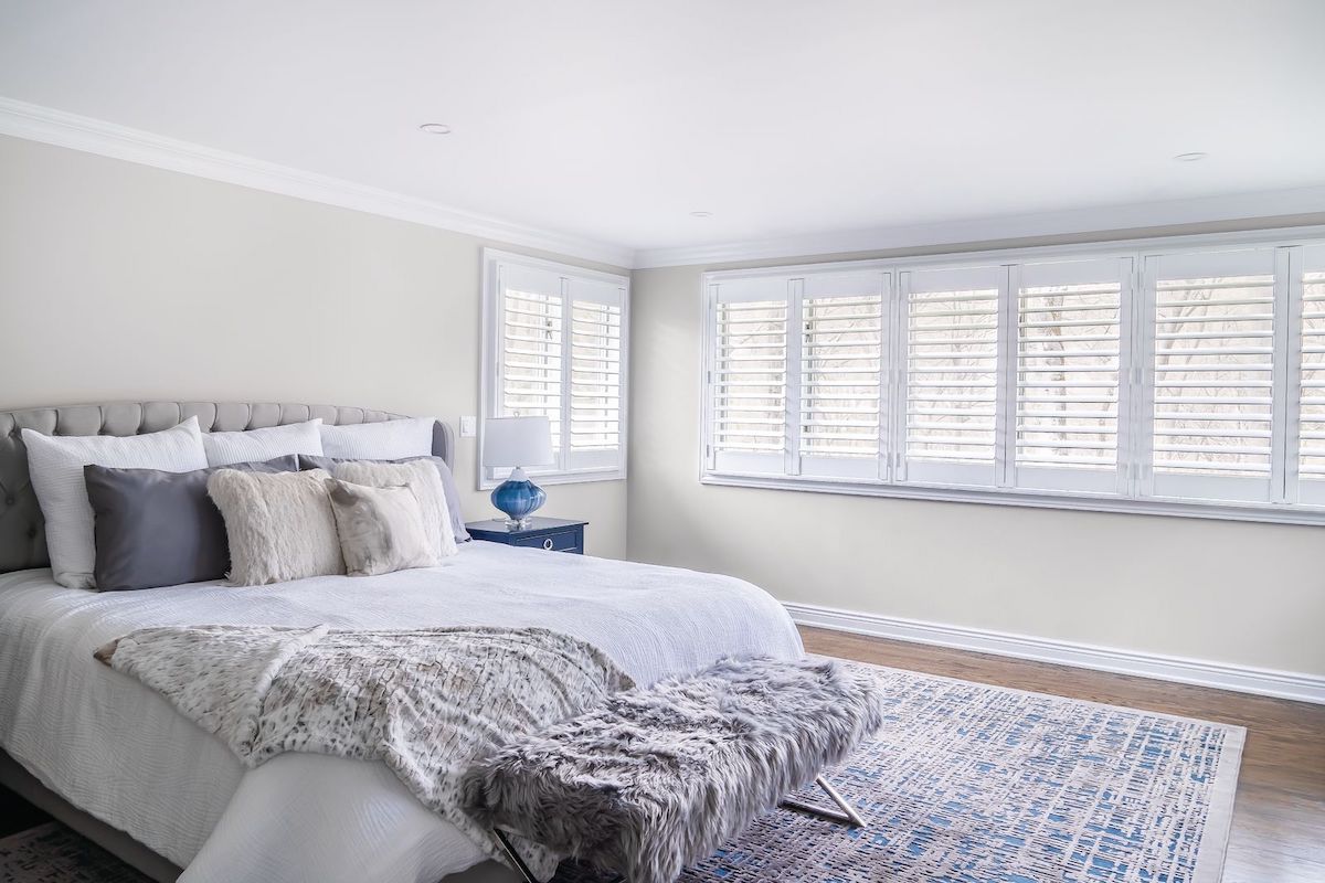 A spacious bedroom features shutters on a long window.