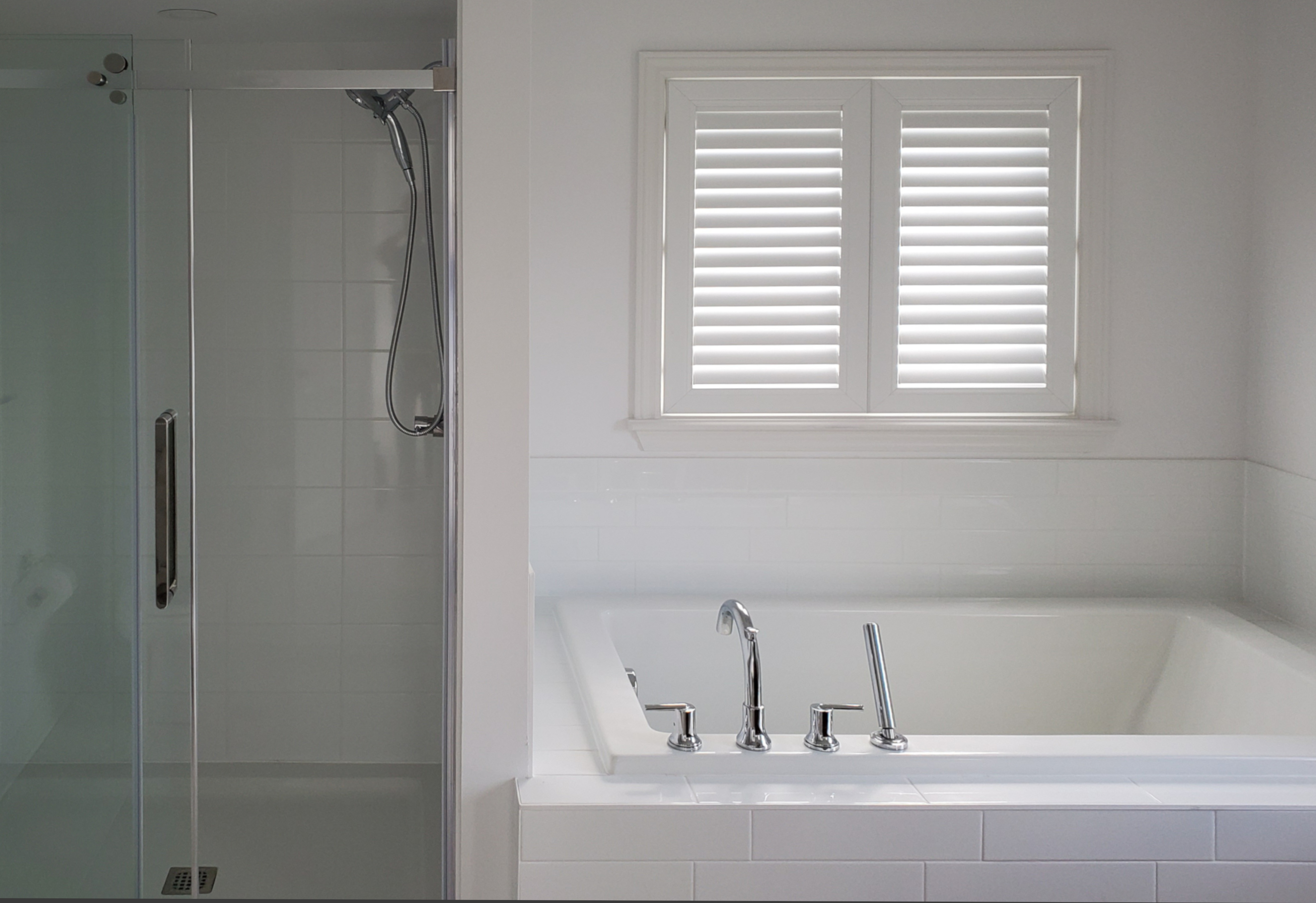 Shutters cover a small window above a standard tub in a bathroom.