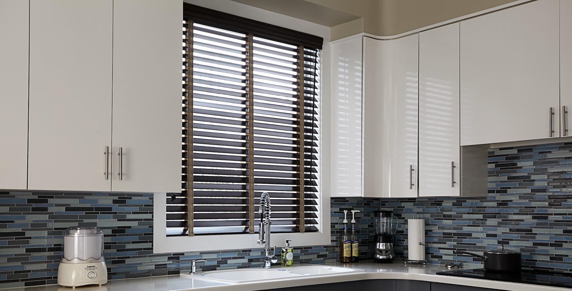 A kitchen window features real wood blinds in a dark brown finish with contrasting tan fabric tape