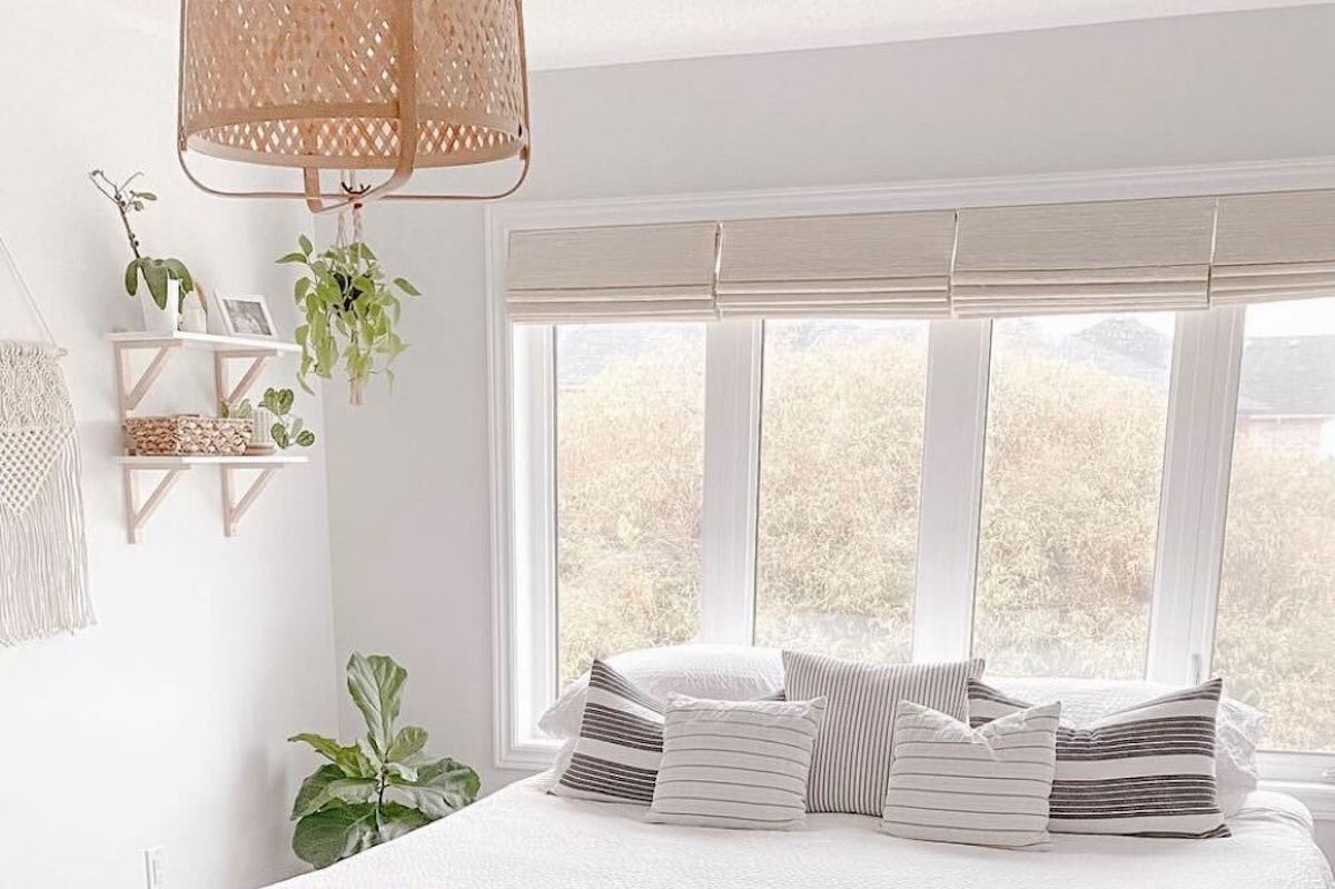 A modern bedroom features four side-by-side windows covered with woven wood shades.