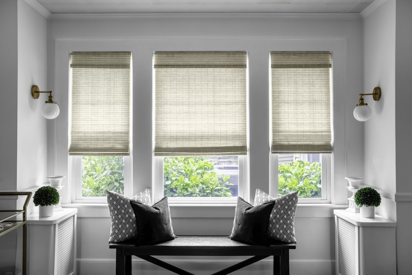Tan woven wood shades cover three windows in a modern entryway.