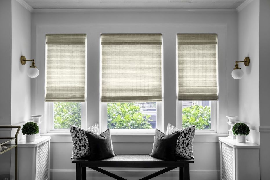 A bay window in a modern home features light tan woven wood shades.