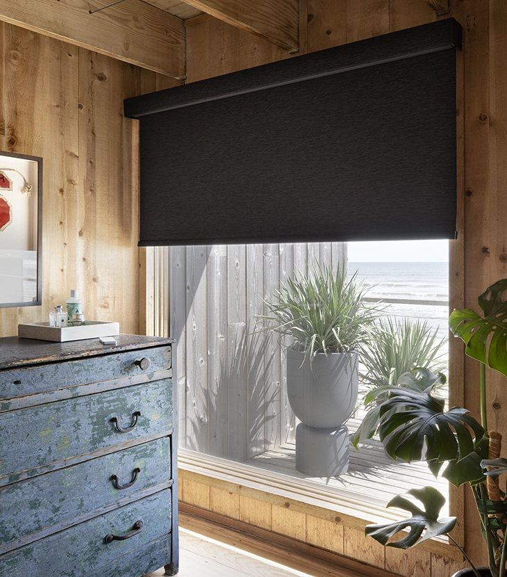 A black roller shade covers a large window in a modern home.