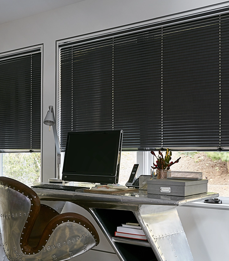 Dark aluminum blinds cover a large window in a modern home office.
