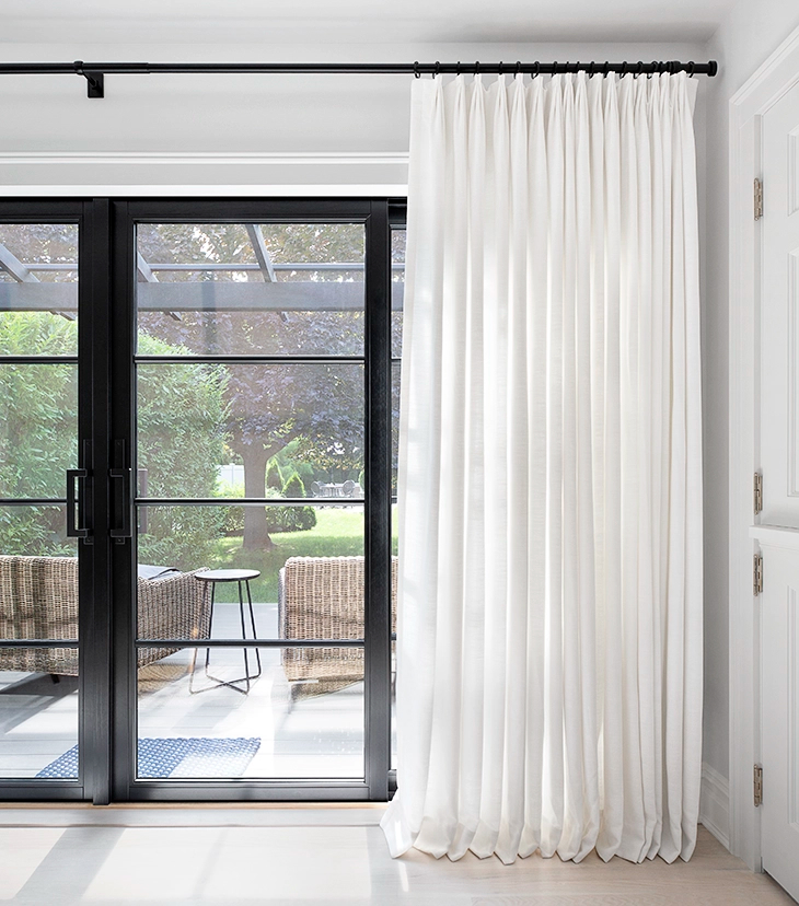 Beautiful, white floor-to-ceiling drapes cover french doors in a modern home.