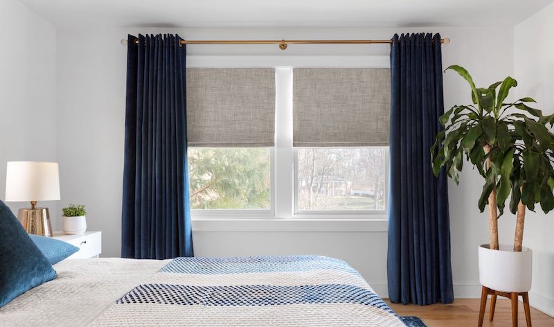 Velvet Drapes in French Blue and Roman Shades cover a large window in a modern bedroom
