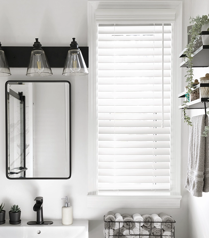 White faux wood blinds cover a narrow window in a bright and modern bathroom.