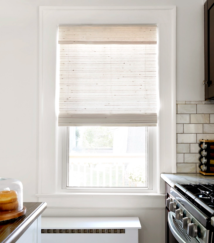 A woven wood shade, partially drawn, allows light to fill a small, modern kitchen.