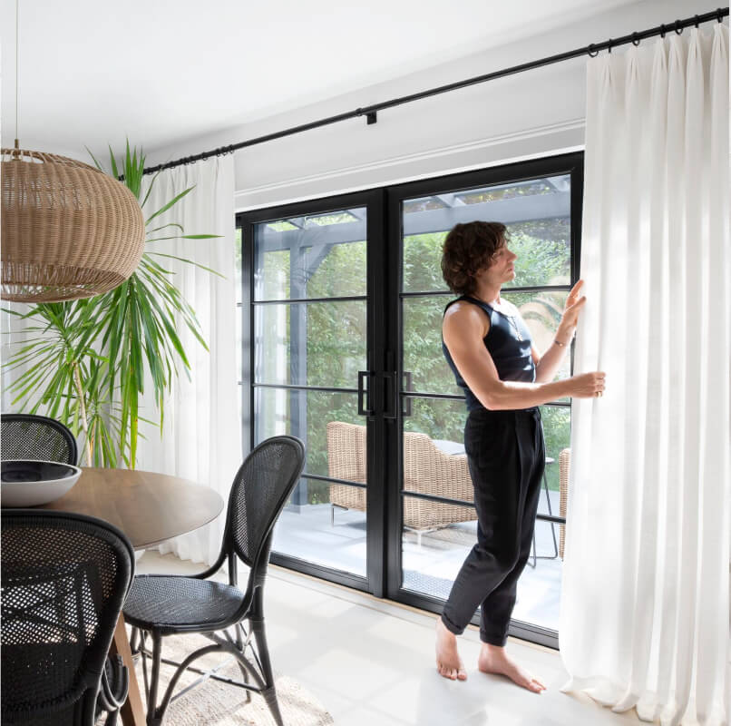 Gregory DelliCarpini Jr. admires white light-filtering curtains on a matte black rod in his contemporary dining room