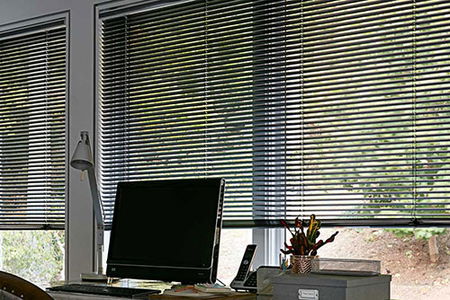 Aluminum blinds cover a large window in a modern home office