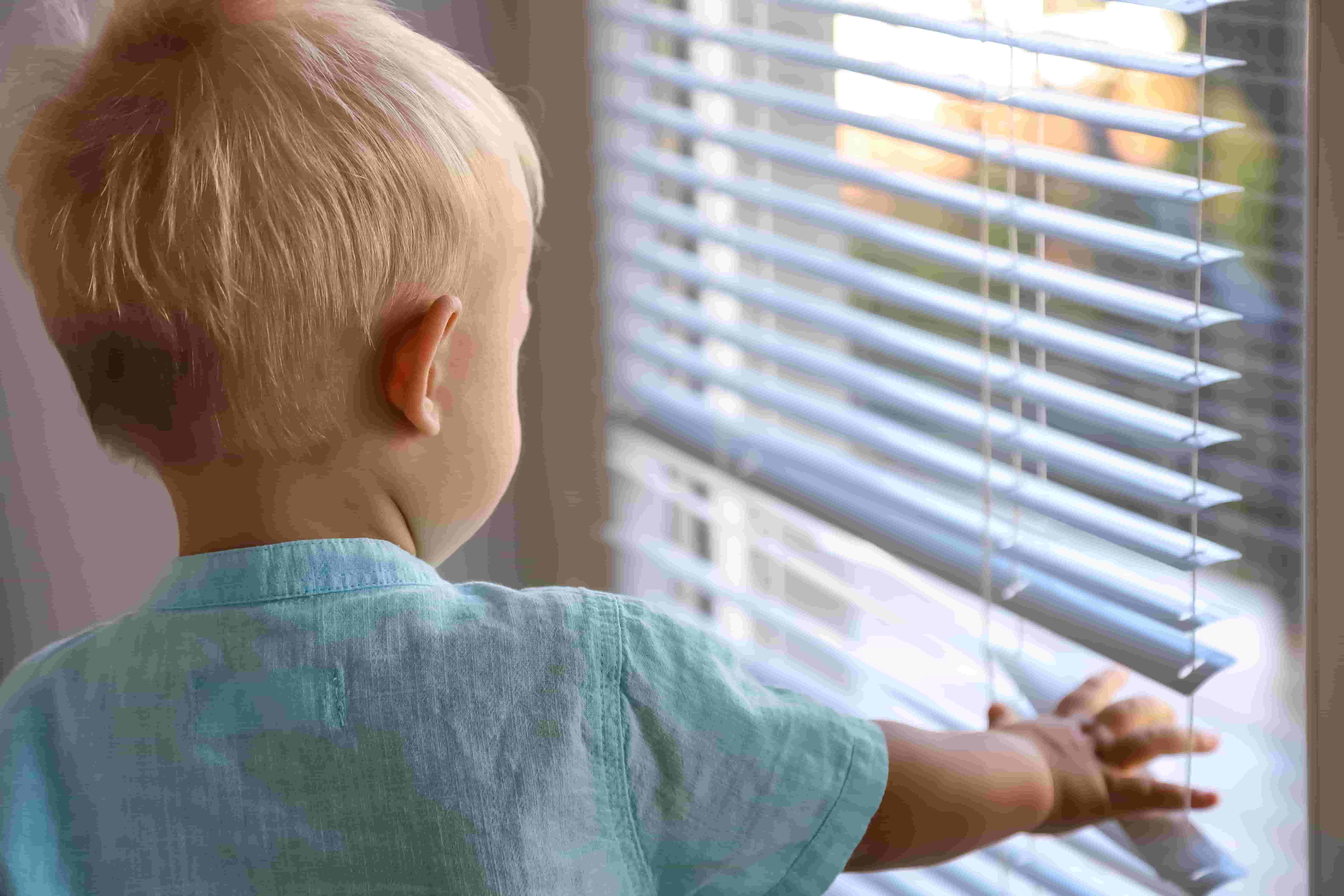 A toddler reaches for aluminum mini blinds A toddler reaches for aluminum mini blinds