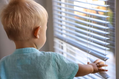 A toddler reaches for aluminum blinds A toddler reaches for aluminum blinds