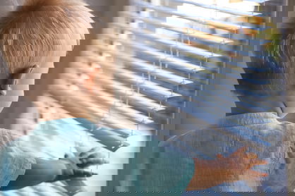 A toddler reaches for aluminum blinds