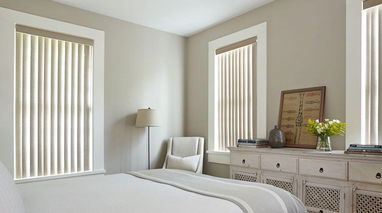 Neutral beige vertical blinds in a cozy bedroom, offering both privacy and soft light filtering.