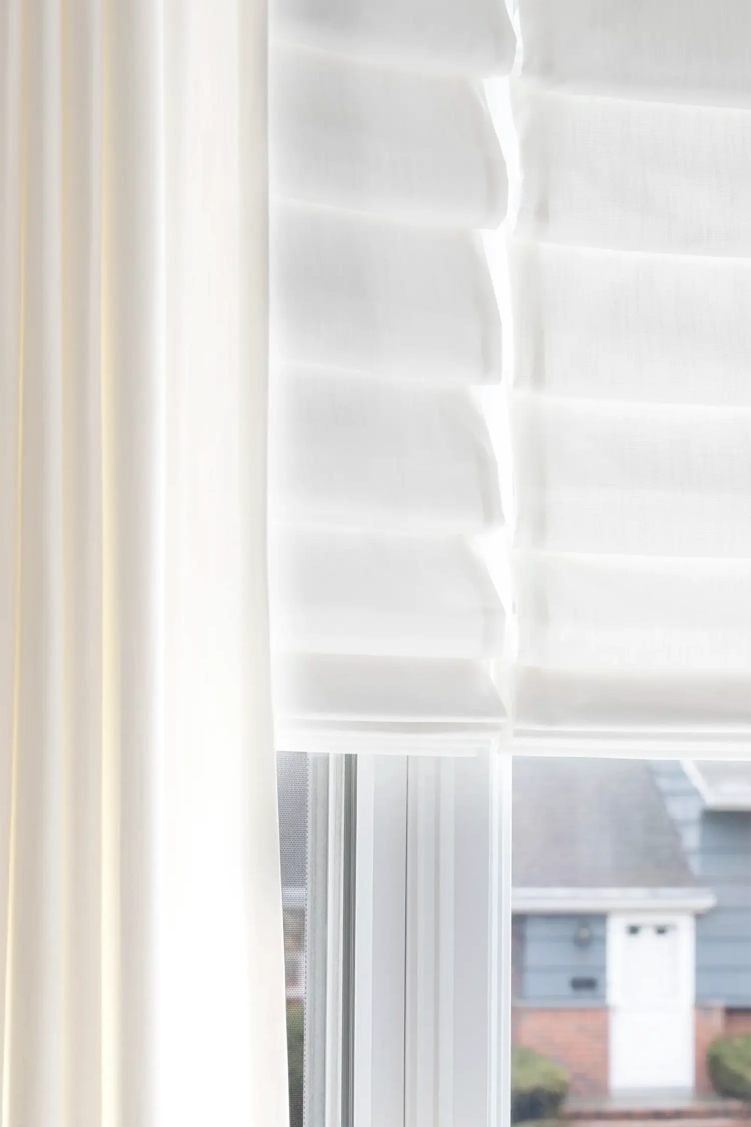 Sheer white drapery beside a roman shade in soft light