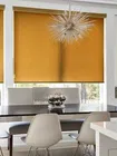 Roller shades in a rich gold color cover large windows in a modern dining room
